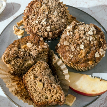 apple cinnamon muffins on a white plate, one cut in half, apple slices.