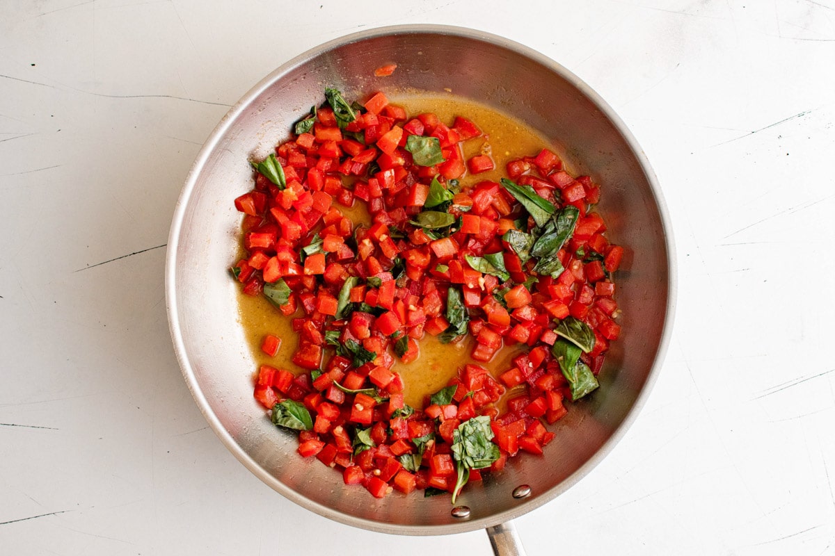 Tomatoes, basil and garlic cooked in a stainless steel skillet.