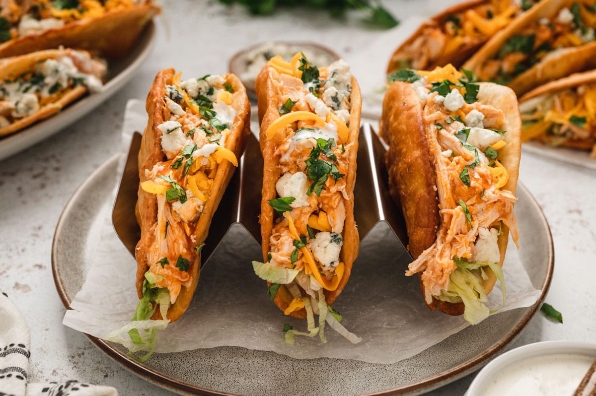 Three buffalo chicken tacos with blue cheese, lettuce and cilantro, lined up in a metal taco holder.