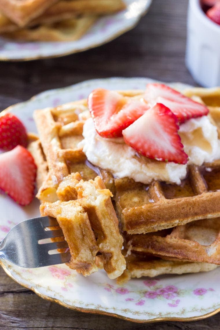 A stack of fluffy buttermilk waffles with a bite taken out. 