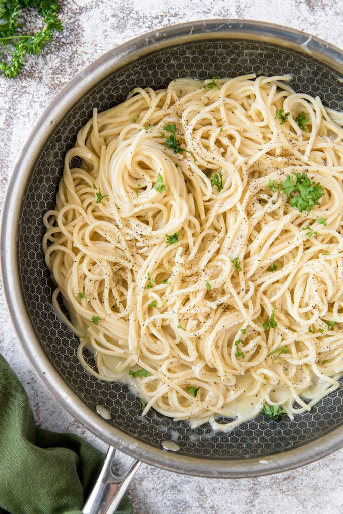 An overhead image of a black skillet with spaghetti noodles and parsley