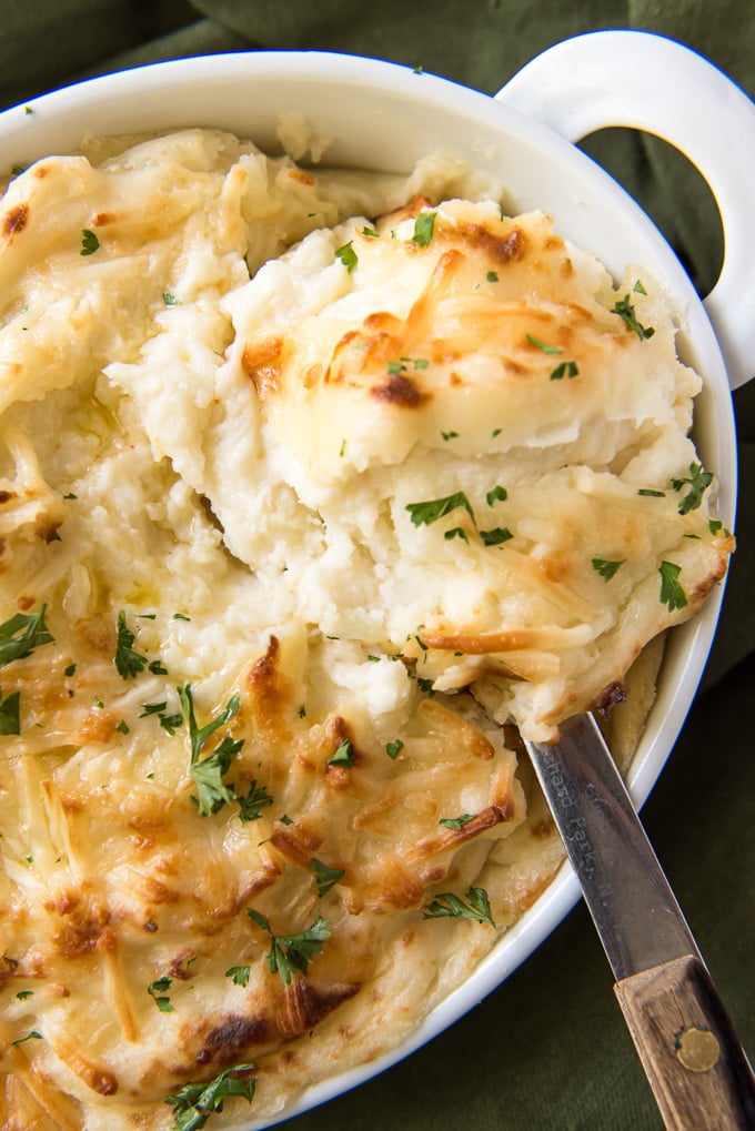 A large spoon with a scoop of cheesy mashed potatoes sitting on the dish