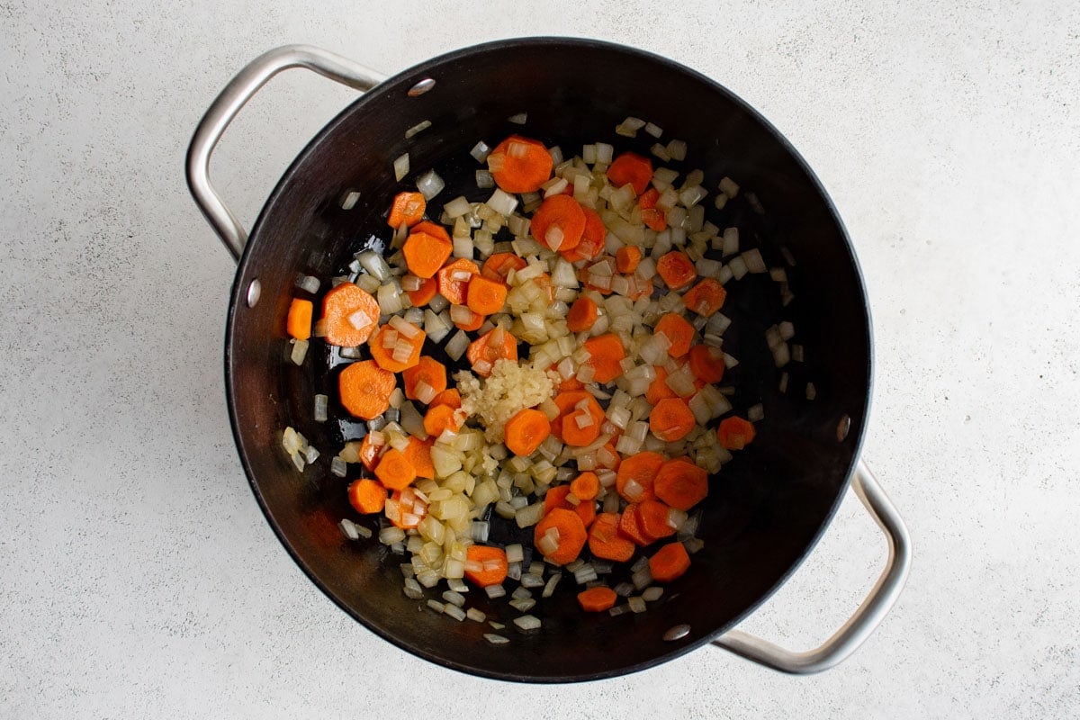 Carrots and diced onions cooking in a large skillet.