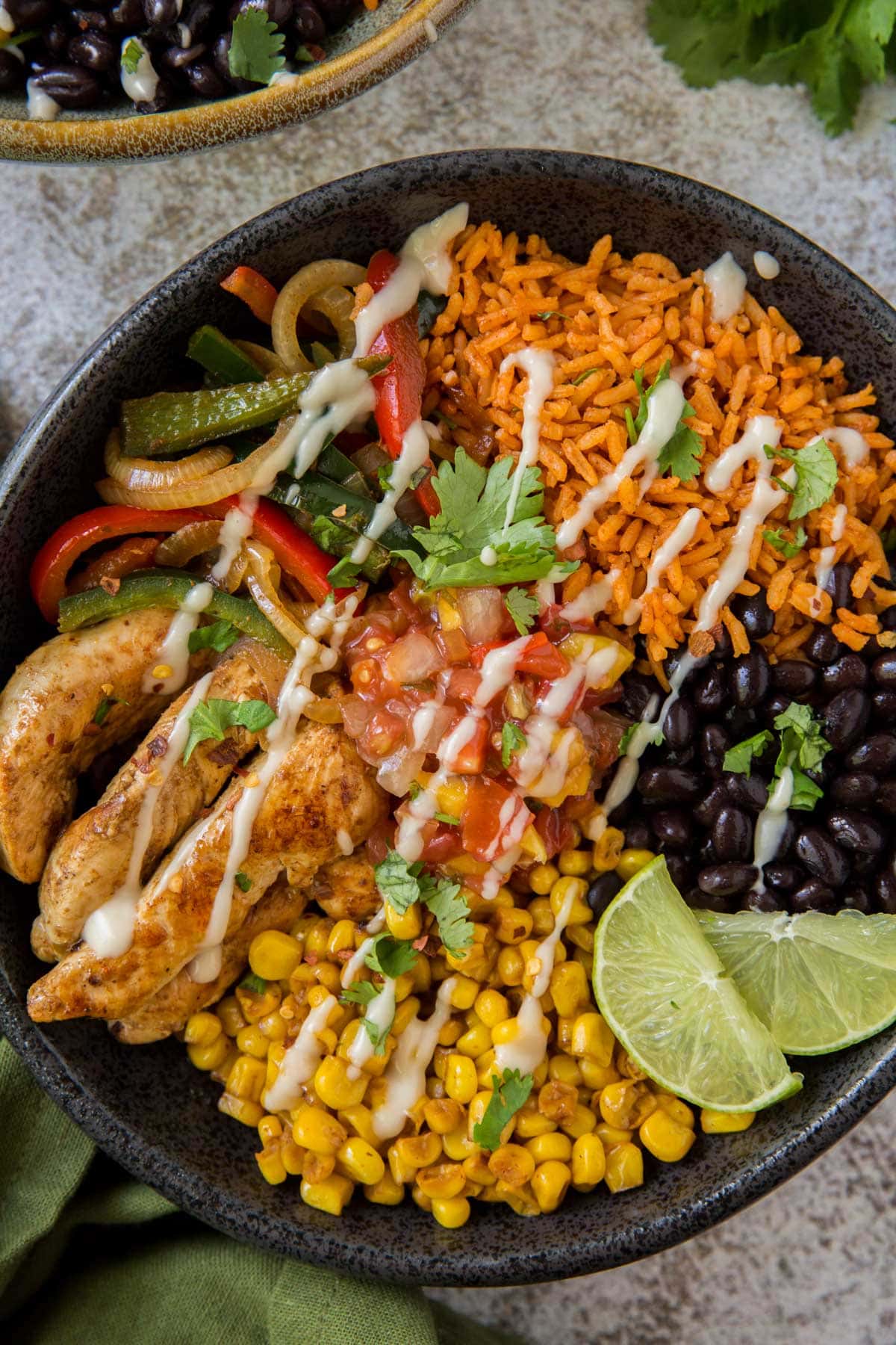 black bowl with chicken fajitas, corn, black beans, peppers and limes