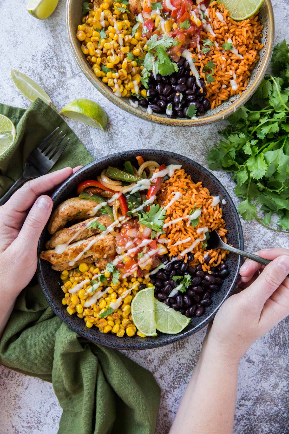 hands holding a black bowl with fajita chicken, rice, limes, beans, and peppers