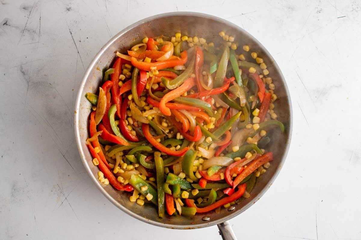 Cooked bell peppers, onions and corn in a skillet.