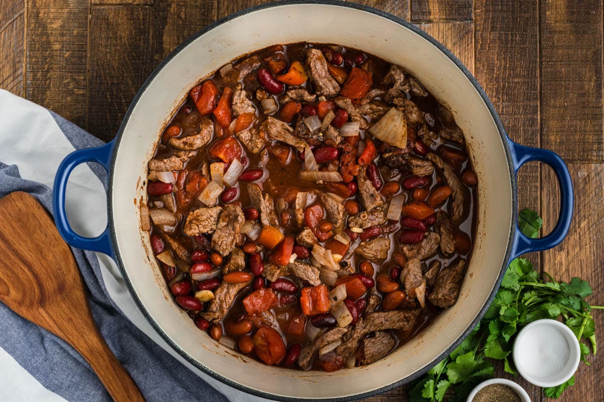 Meat, tomatoes, onions and beans in a dutch oven.