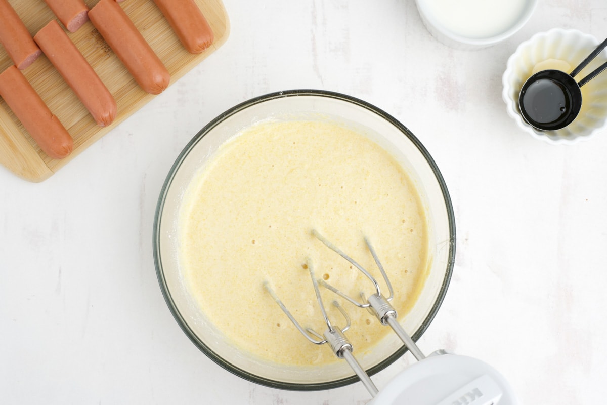 Yellow batter in a glass mixing bowl with a hand mixer.