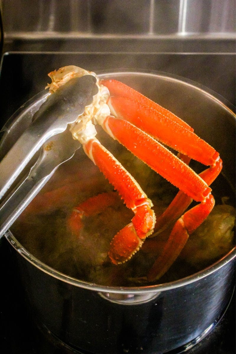 tongs lifting crab legs out of a pot of water