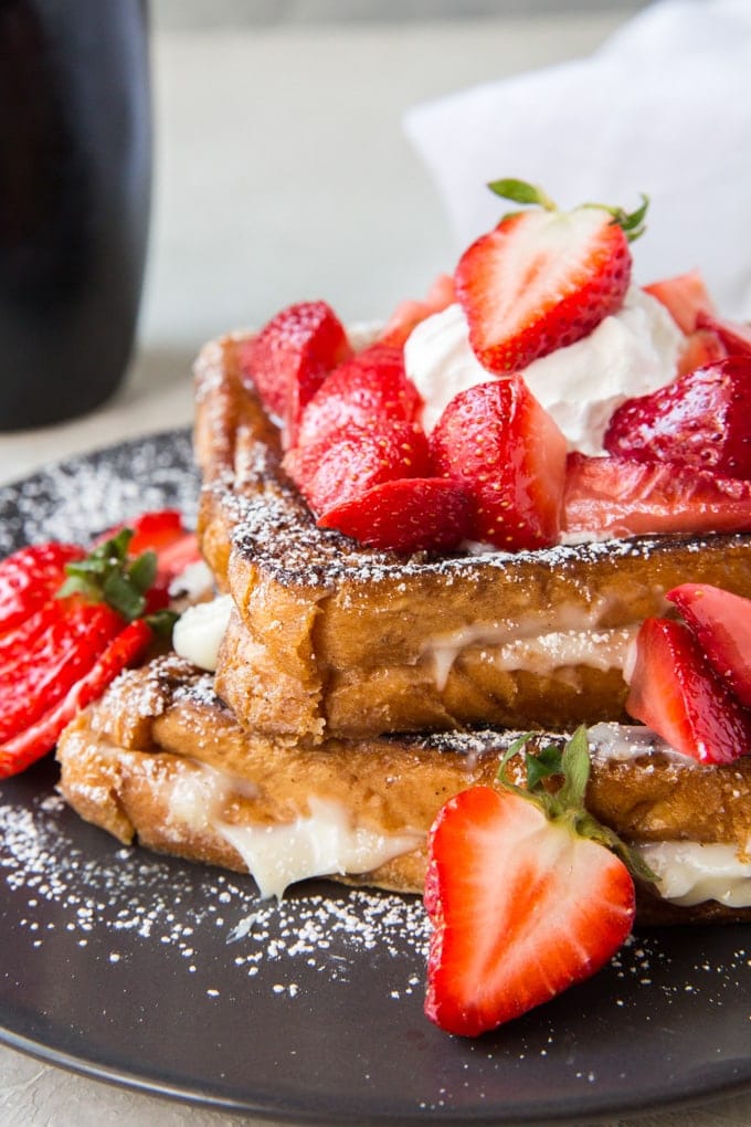 Two slices of french toast with a sweet cream cheese filling and topped with powdered sugar and strawberries.