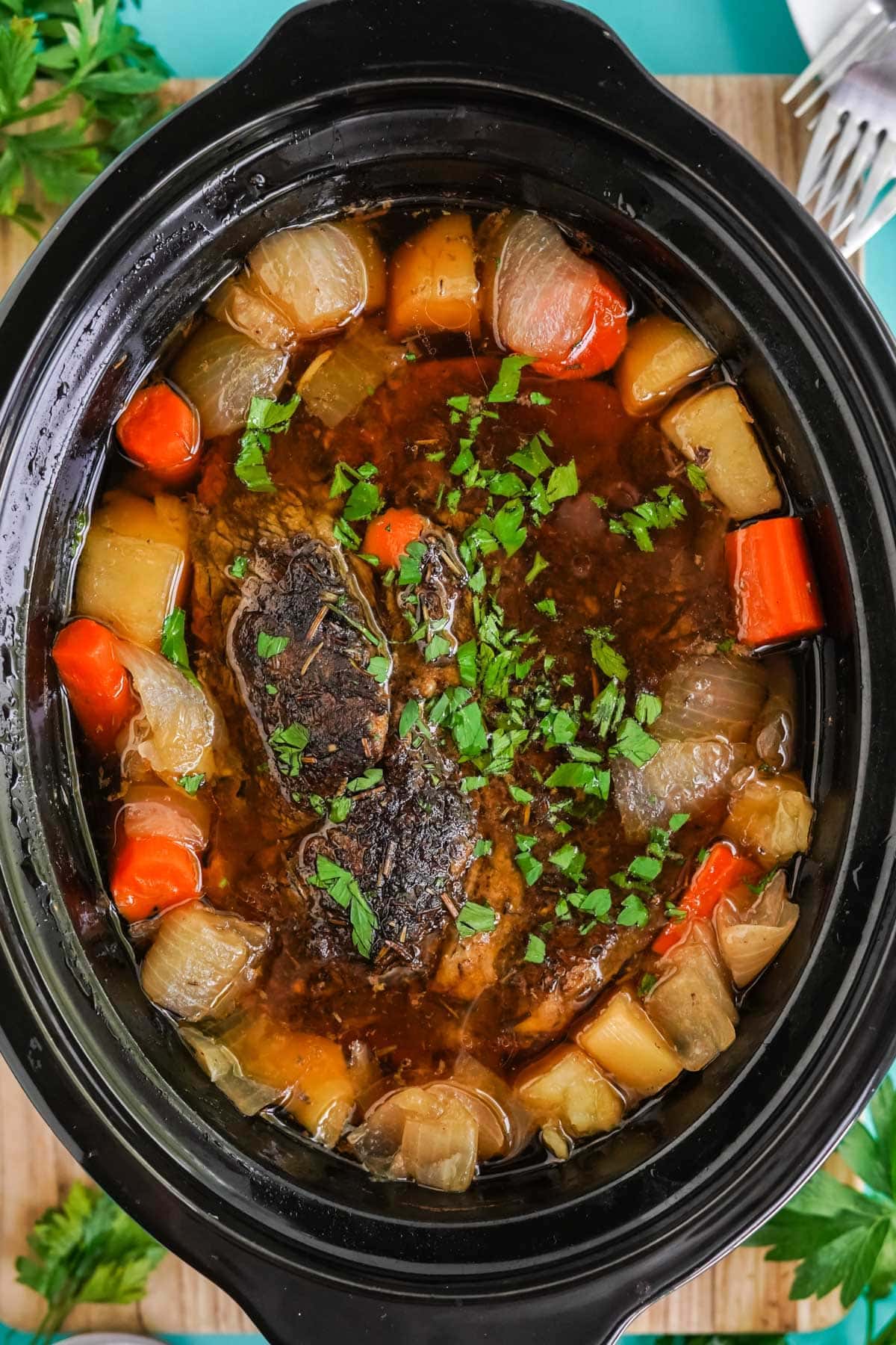 chuck roast in a slow cooker surrounded by potatoes and carrots with parsley on top