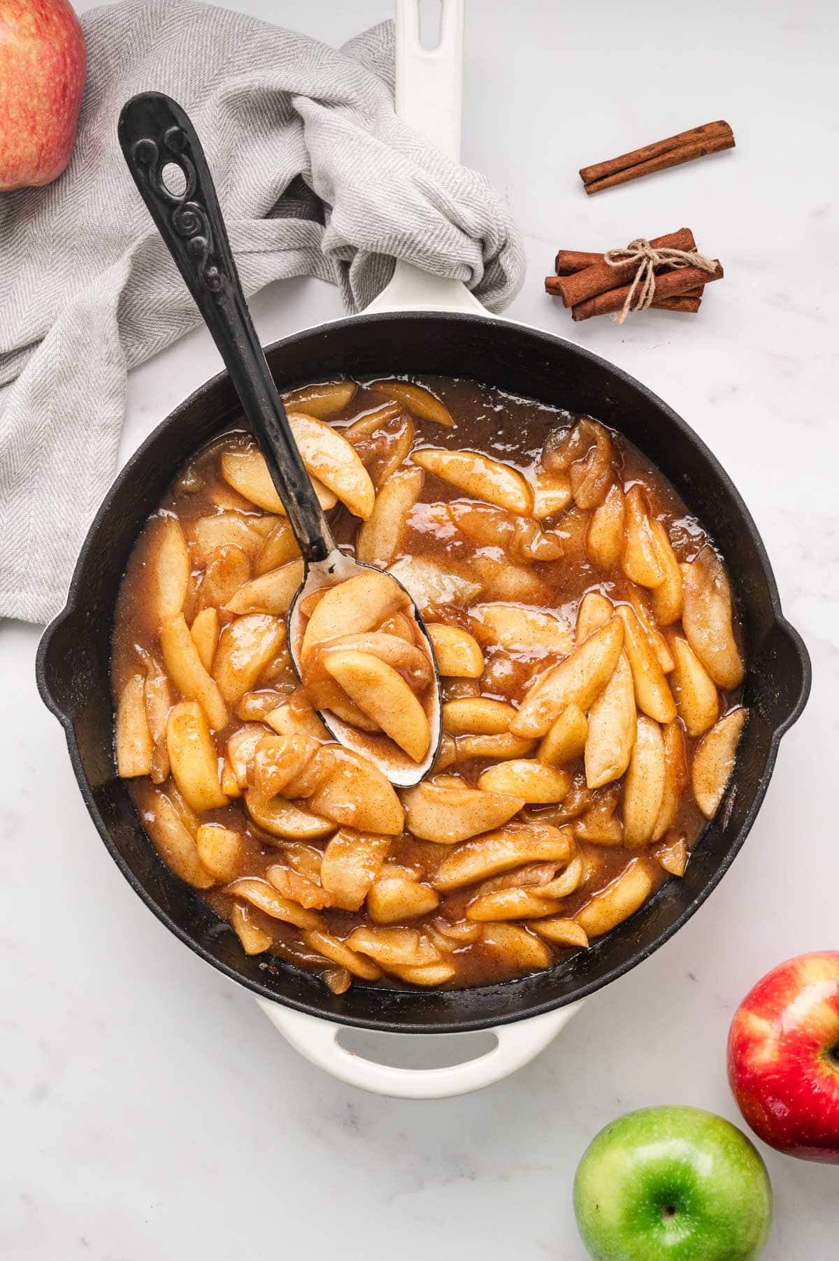 Fried apples in a large skillet with a serving spoon.