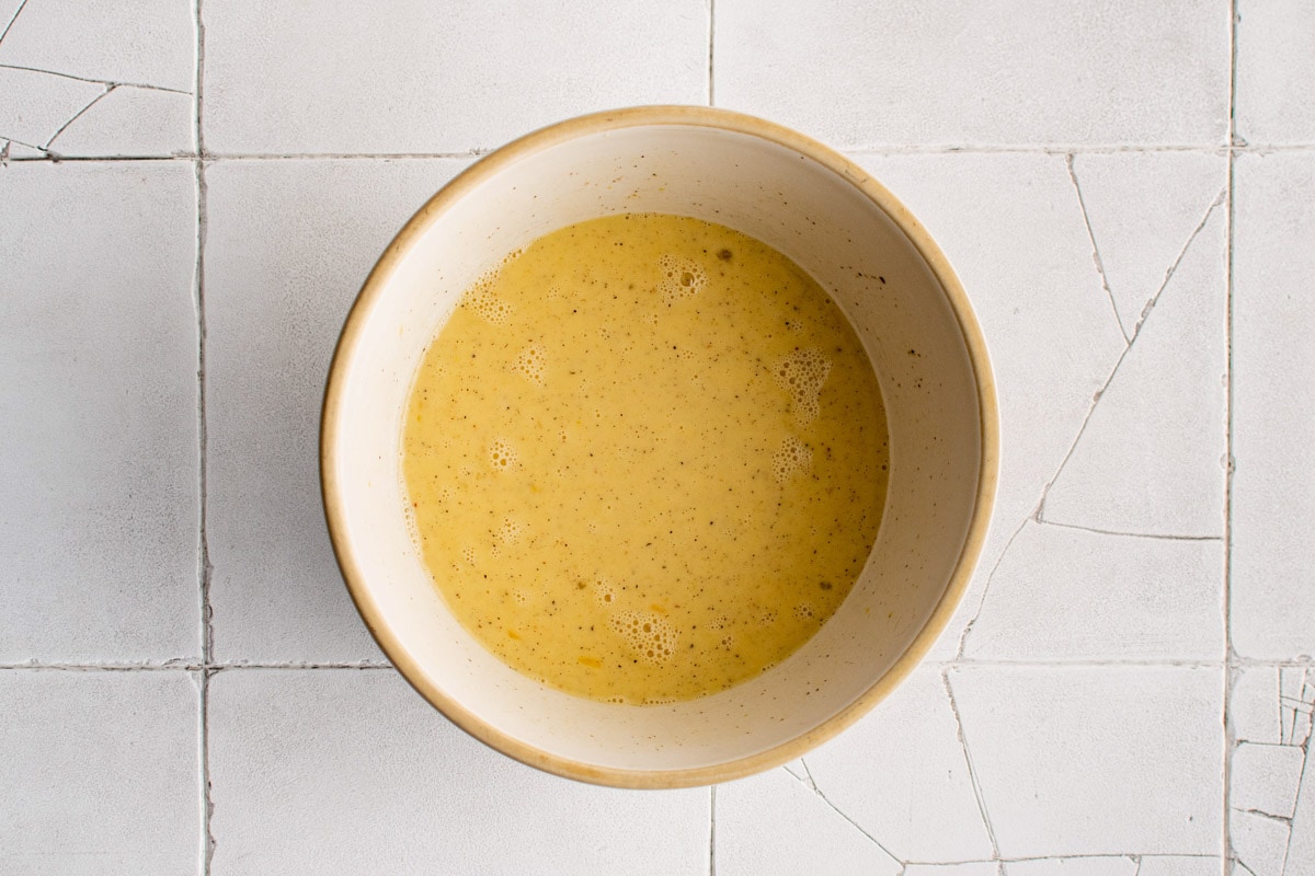 Eggs whisked in a bowl with seasonings.