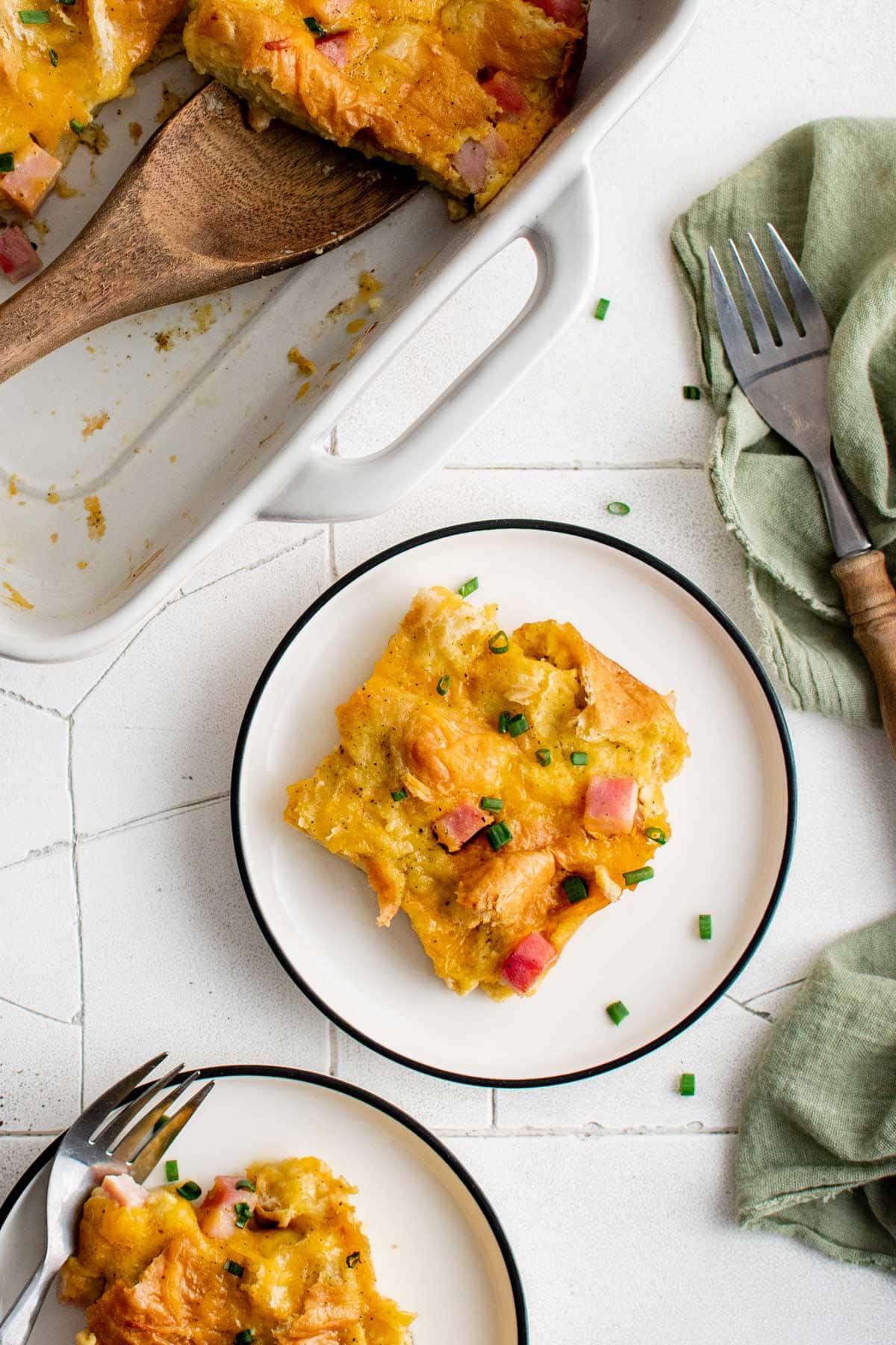 Square servings of breakfast croissant casserole on white plates.