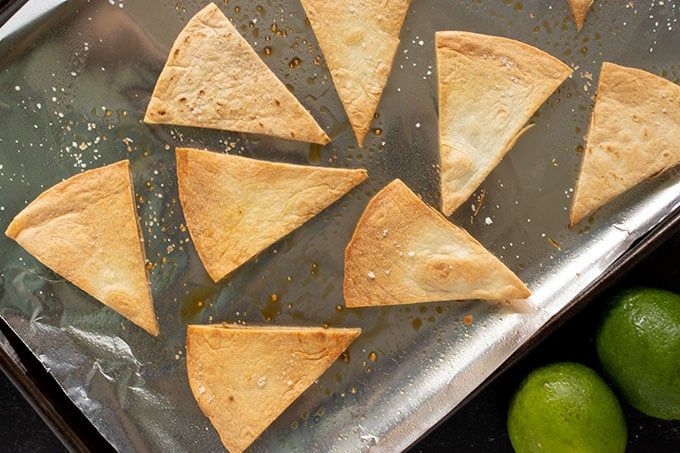 homemade tortilla chips on baking sheet with foil, two limes