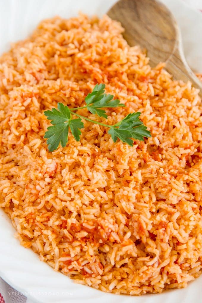 Authentic Mexican Rice recipe on a platter with a wooden spoon, a sprig of parsley
