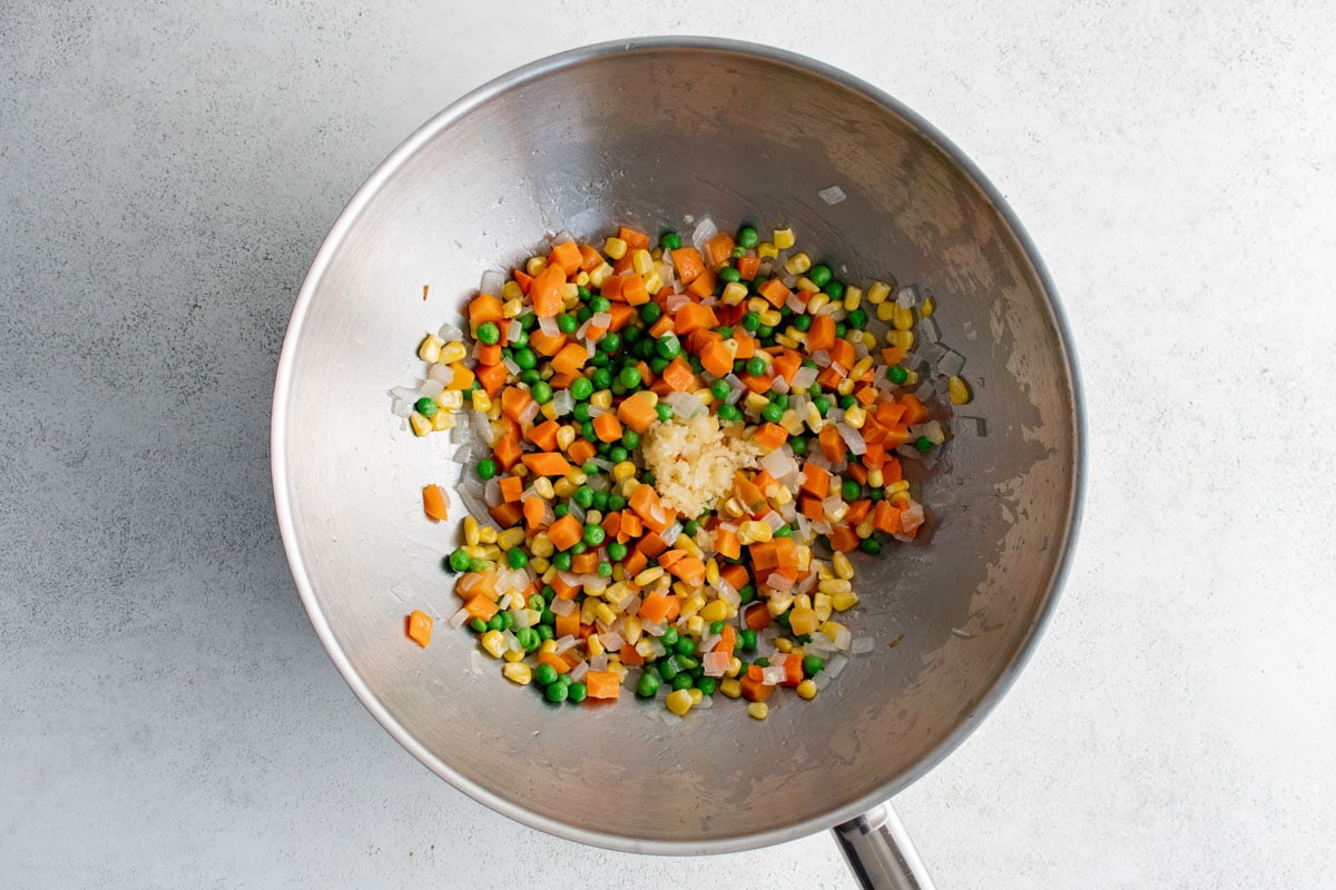 Peas, carrots, garlic and corn in a wok.