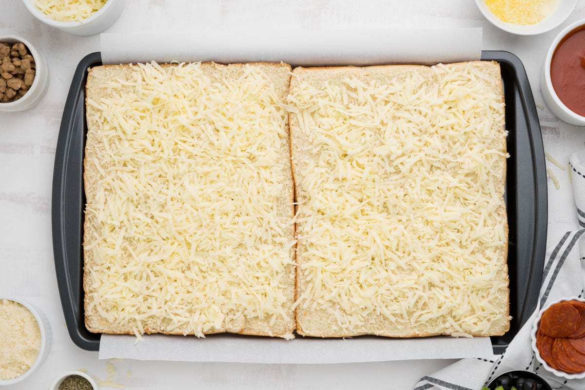 Two bottom slabs of hawaiian rolls with shredded cheese.