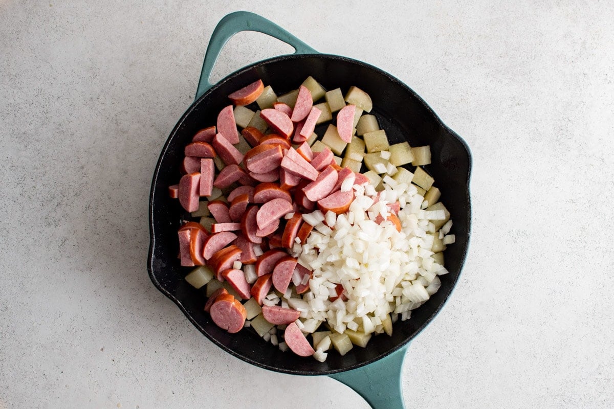 Sausage an onions over potatoes in a skillet.