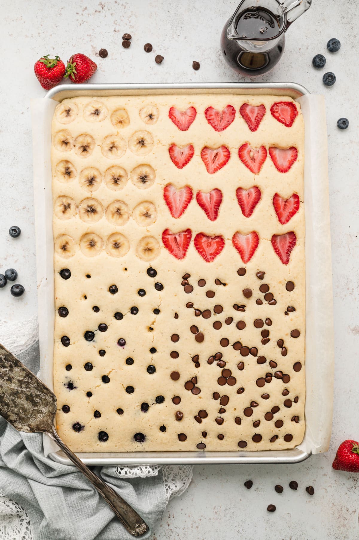 Sheet pan pancake with bananas, blueberries, strawberries and chocolate chips each in it's own quadrant.