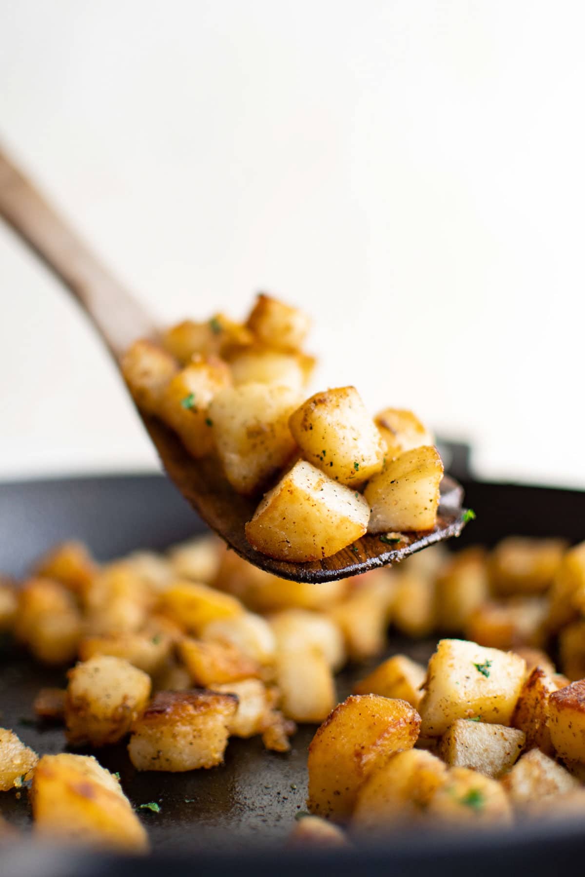 Wooden spoon with a serving of skillet potatoes over a cast iron skillet. 