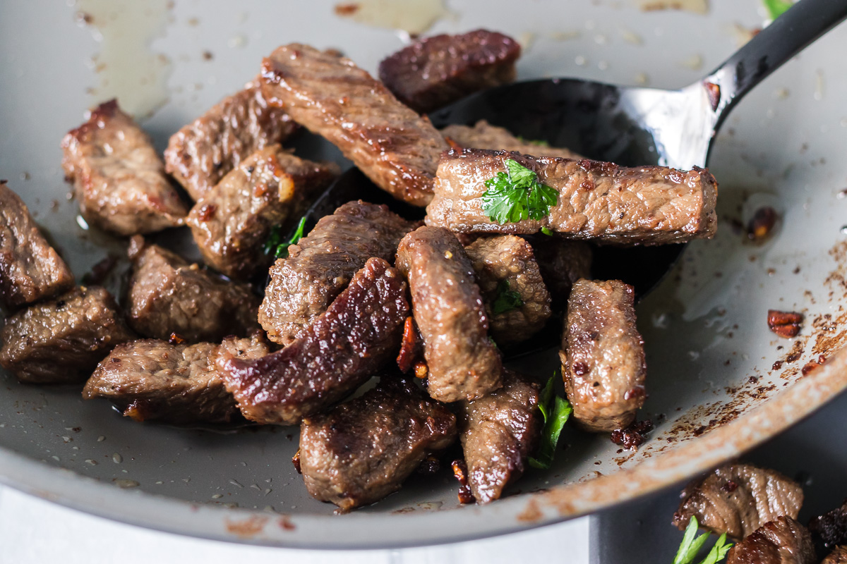 small pieces of steak in a skillet with a spoon