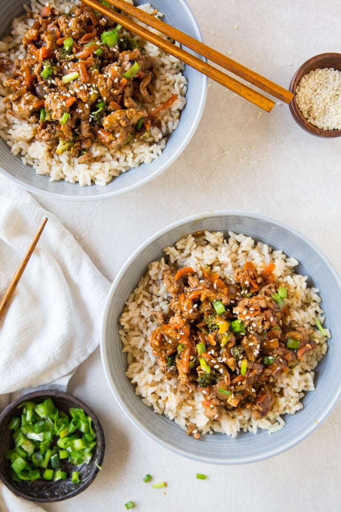 light gray bowls with rice and healthy ground turkey teriyaki, chopsticks, sesame seeds, white napkin, green onions